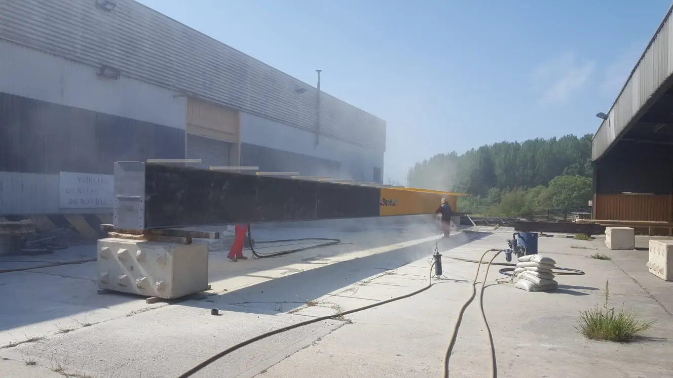 Steel beams being blasted outdoors, typical of shot blasting in Consett